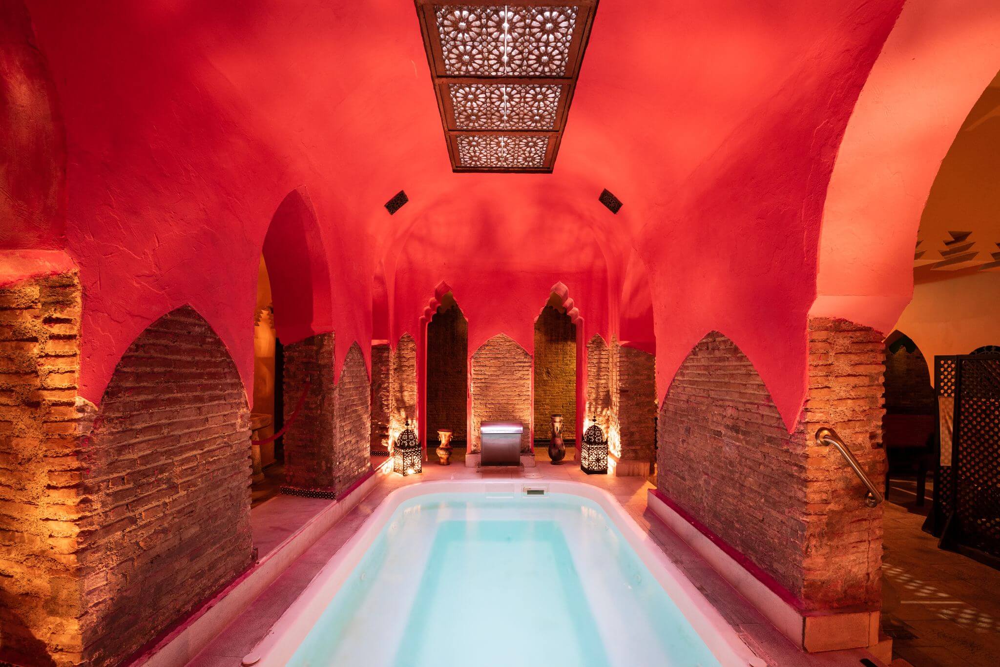 inside a dimly lit hammam with a pool in the centre, surrounded by red walls