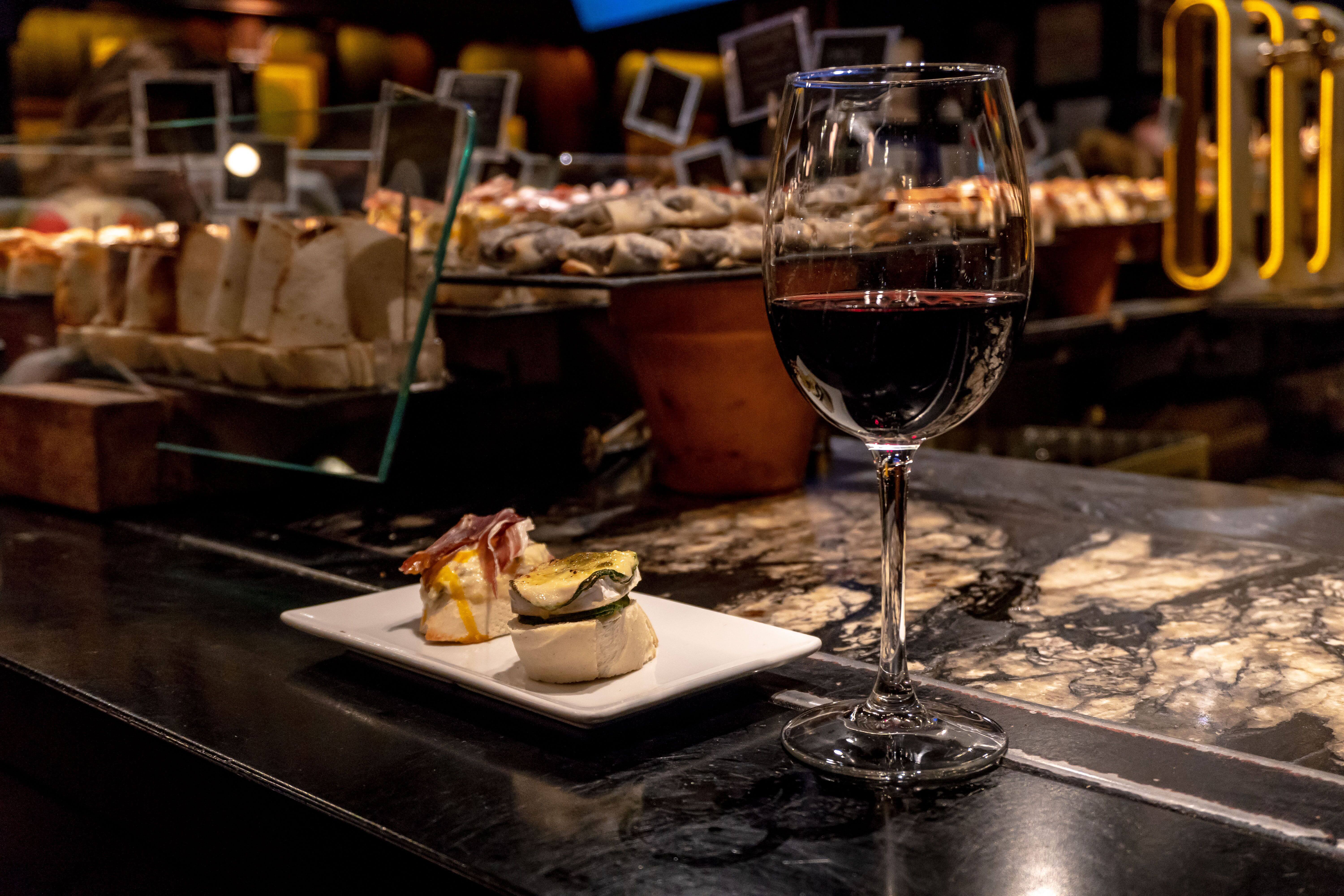 a glass of red wine and small plate of tapas in dimly lit bar