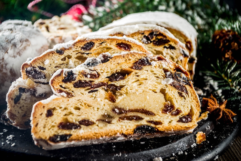 slices of stollen dusted with flour on a black plate surrounded by festive table adornments