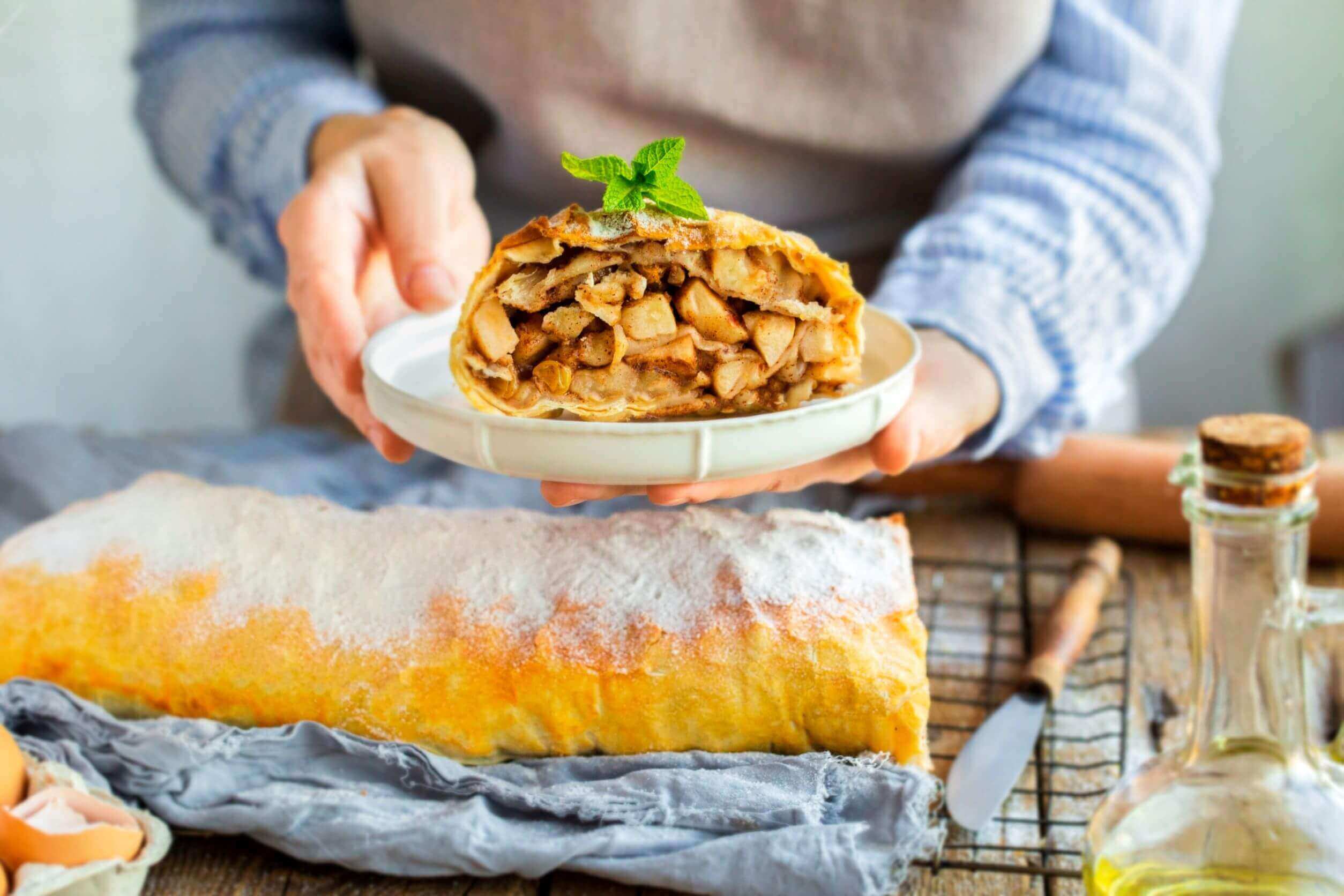 close up of delicious apple strudel on a plate, held by a person in a blue shirt