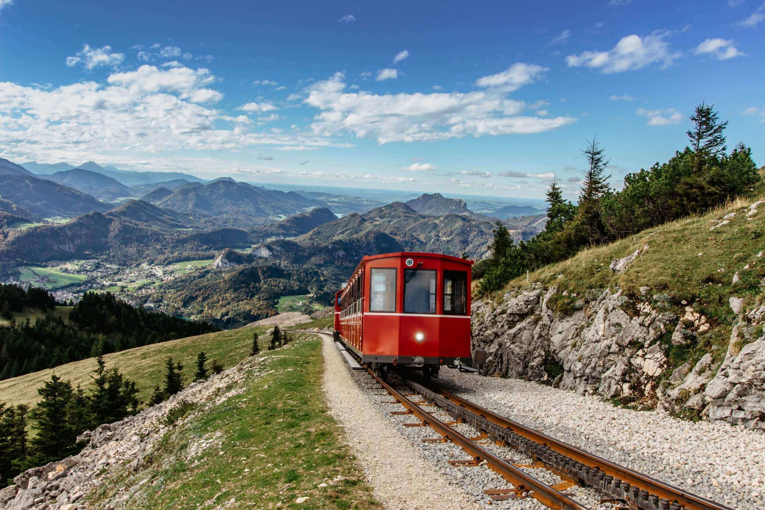 red train carriage along a train track on a hill with mountains in the background