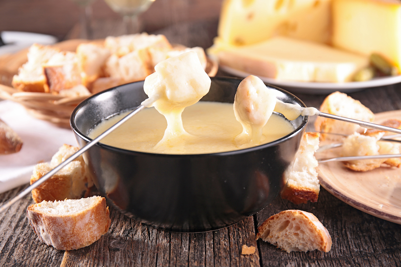 slices of bread on a pair of skewers being dipped into a steaming pot of cheese fondue