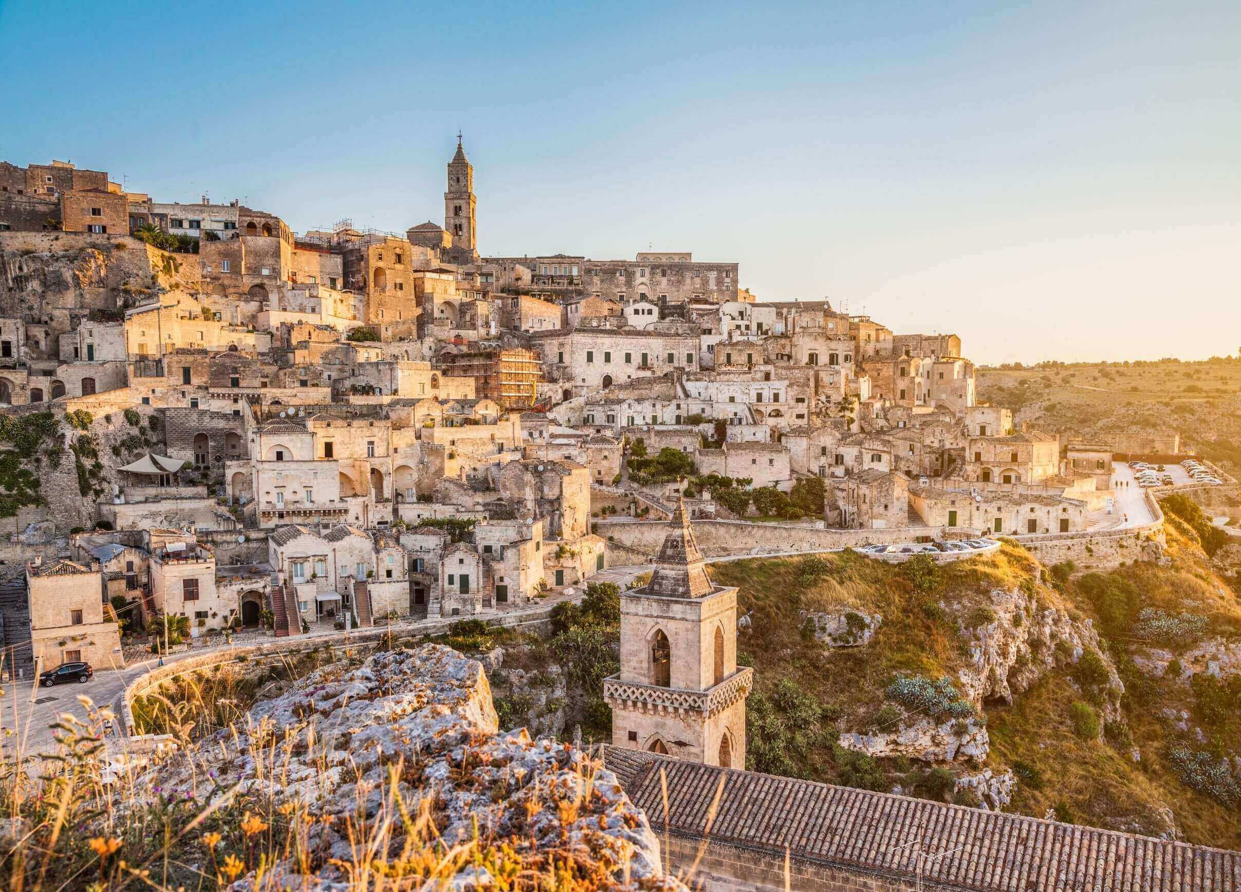 UNESCO world heritage site of Matera Sassi Caves stacked on top of one another under blue skies and a sunlight in the distance