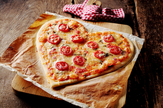 a heart shaped margherita pizza on a wooden board and rustic wood table