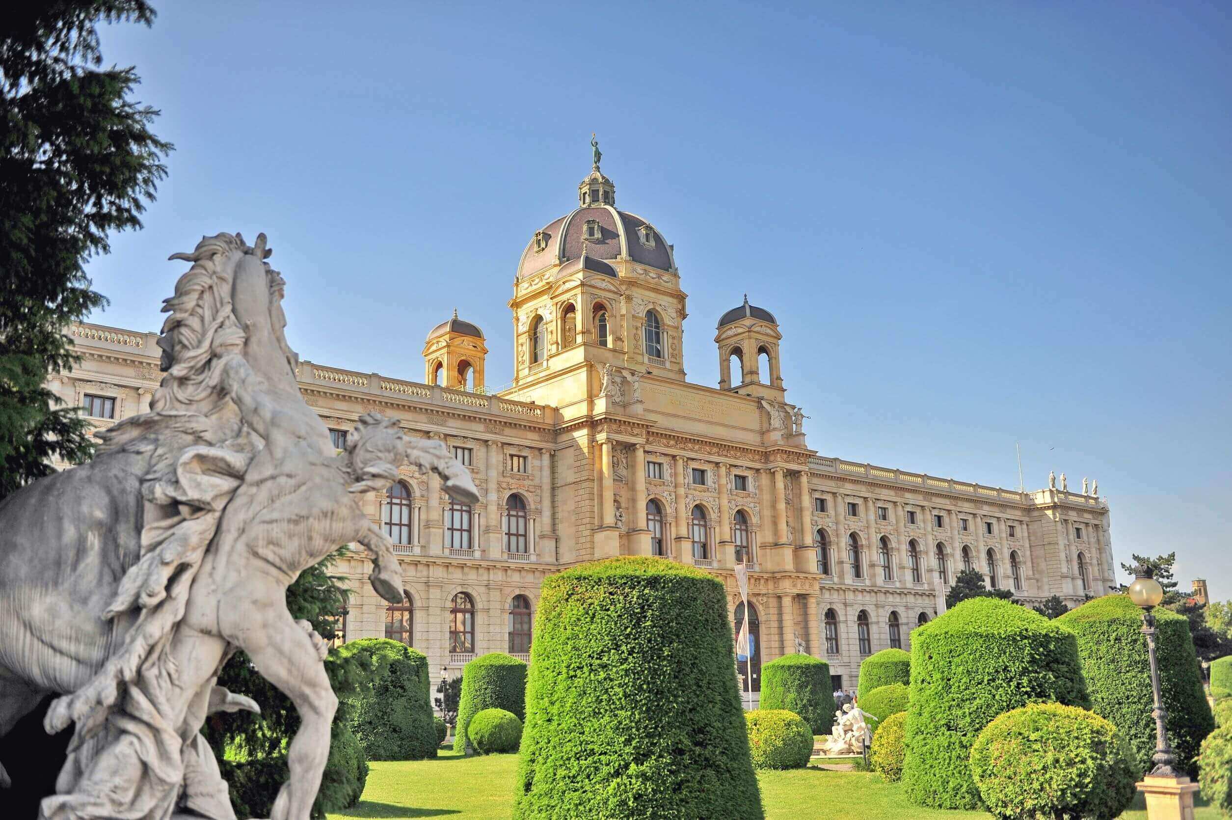 slight low angle wide shot of the Arts History Museum in Vienna, Austria with trimmed green hedges and horse statue