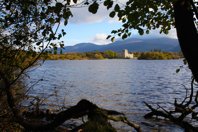 view of the Lakes of Killarney in southern Ireland through the frame of trees with blue skies and clouds