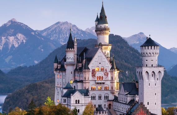 A white castle stands amongst mountains in Europe.