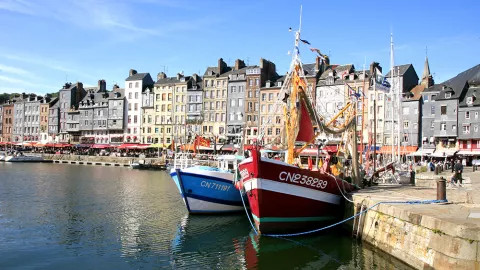 Impressive buildings line the Honfleur waterfront, with two boats in the foreground.