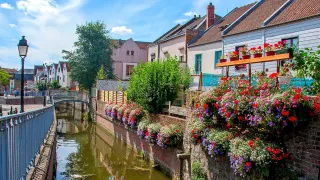 A view of the town of Amiens, with a river flowing through next to flower adorned houses.