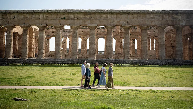 A group of travellers walking around a site with old Italian ruins.