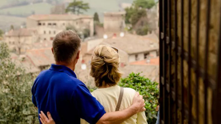 middle aged couple facing with backs to camera and arms around one another looking out over an Italian village skyline