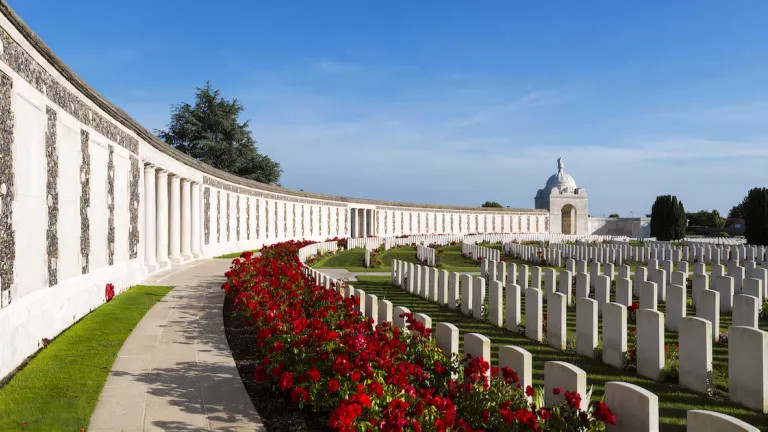 Tyne Cot Commonwealth War Graves Cemetery, Ypres, with blue sky and red flowers