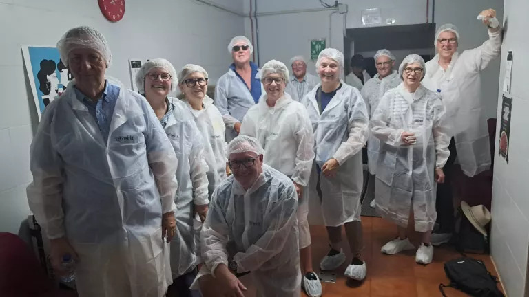 A small group of mature people wearing white overcoats and smiling at the camera.