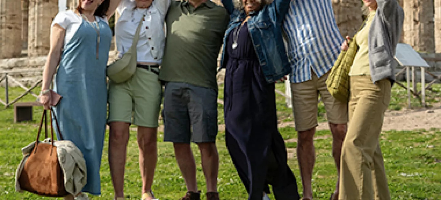 A group of travellers pose for a photo in front of Italian ruins. 