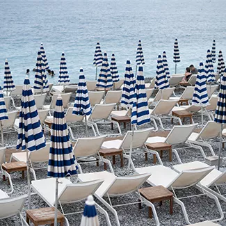 A beach in France with rows of white lounge chairs and blue-and-white striped umbrellas.
